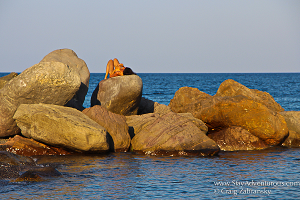 sun bathing on the rocks at the black sand beach of Kamari in Santorini, Greece