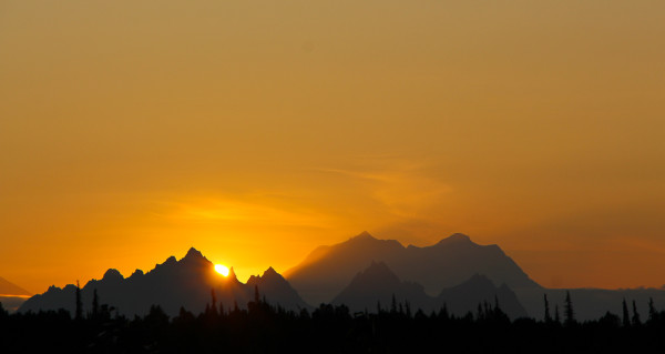 sun hiding behind the Alaskan Mountain Range near Denali in Alaska